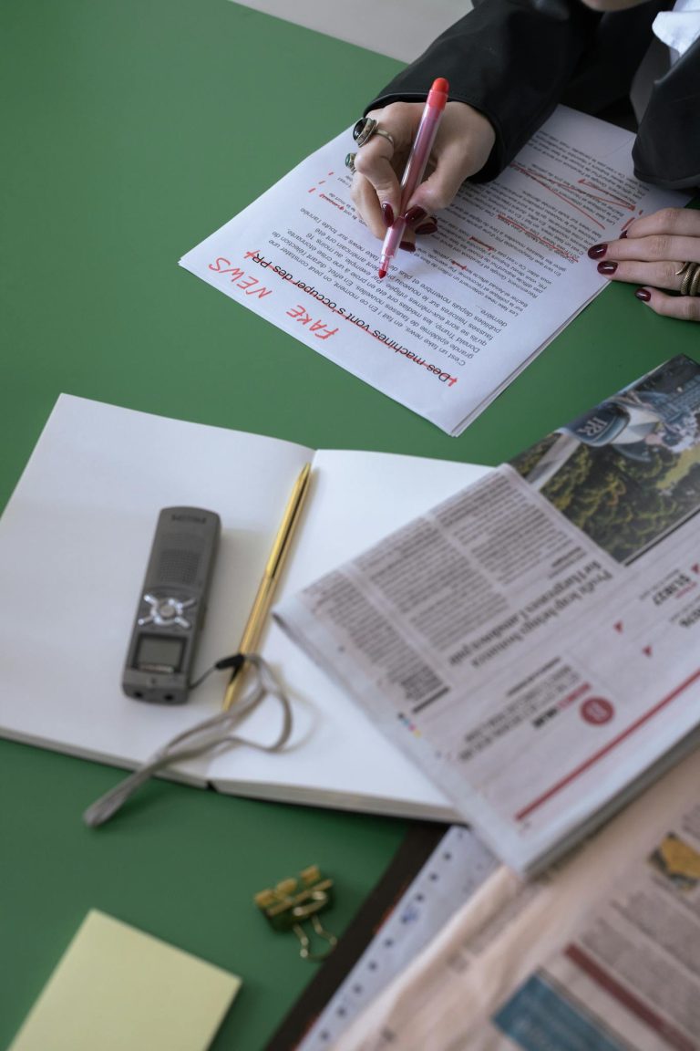 An overhead view of a person editing newspapers and documents at a desk.
